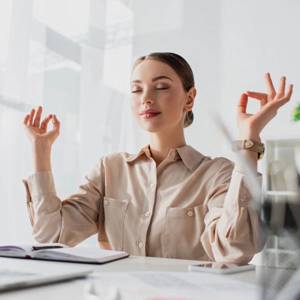 Femme pratiquant la méditation au travail devant son ordinateur pour réduire le stress.