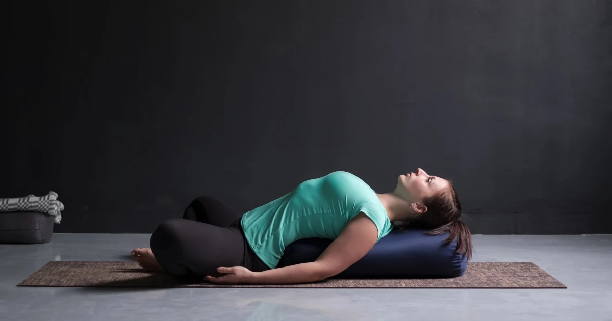 Femme allongée sur un bolster dans une posture de détente, illustrant les effets du yoga anti-fatigue pour relâcher les tensions et calmer le système nerveux.