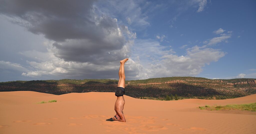 Sirsasana, posture de yoga sur la tête pratiquée en extérieur sur du sable, avec instructions et bienfaits.