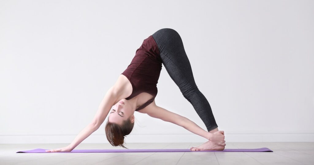 Pratiquante réalisant une posture de yoga en torsion debout, tenant son pied avec la main opposée sur un tapis de yoga.