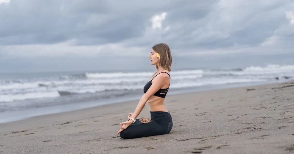 Femme méditant sur une plage au bord de la mer au coucher du soleil, pour illustrer la formation en méditation.