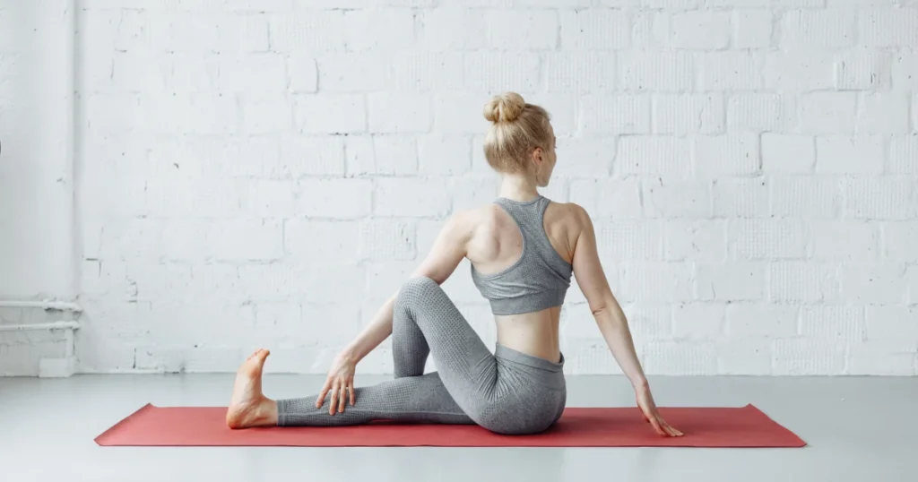 Pratique de yoga pour le dos : Femme en torsion assise (Ardha Matsyendrasana) sur un tapis rouge, dans un espace lumineux, illustrant les bienfaits du yoga pour la colonne vertébrale.