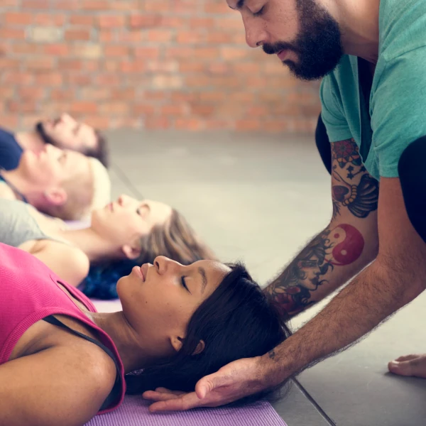 Professeur de yoga guide un élève dans la posture de Savasana, position de relaxation profonde en fin de séance.