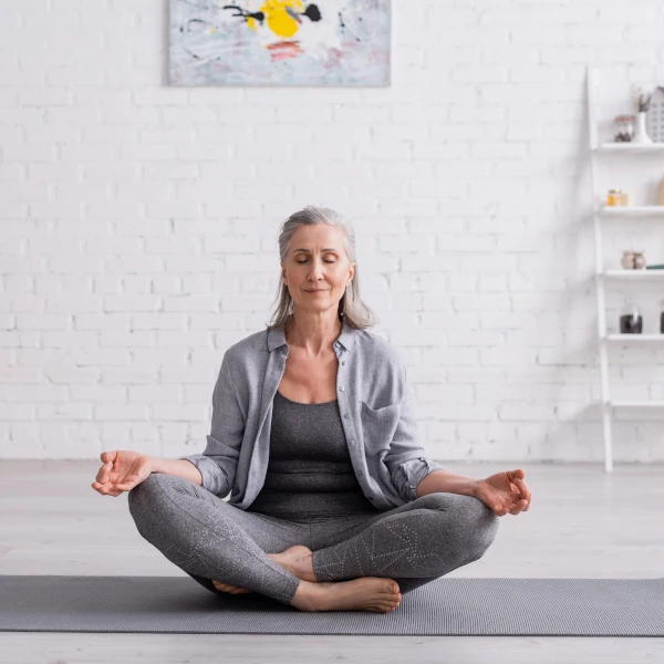 Femme en méditation de pleine conscience assise sur un tapis, pratiquant une séance guidée dans un espace calme.